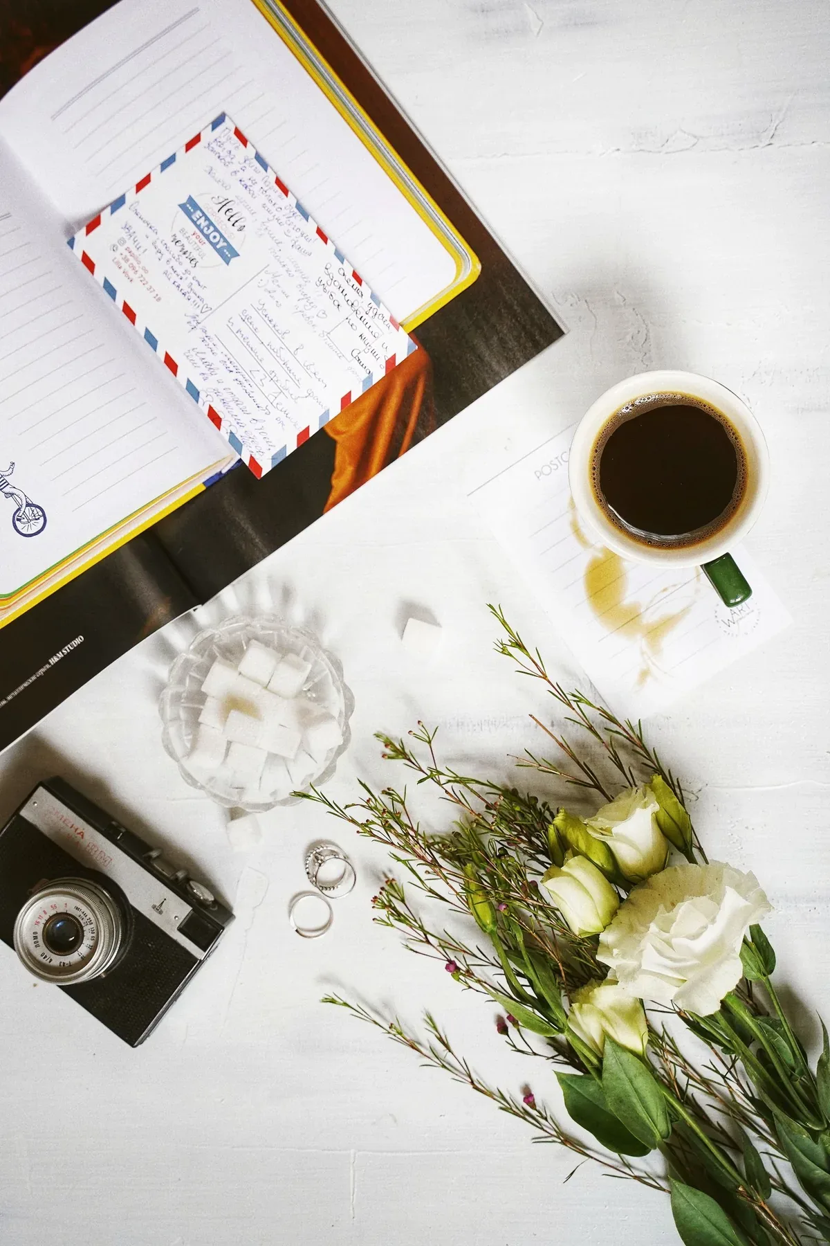 A journal, coffee, flowers, and camera arranged on a bright table