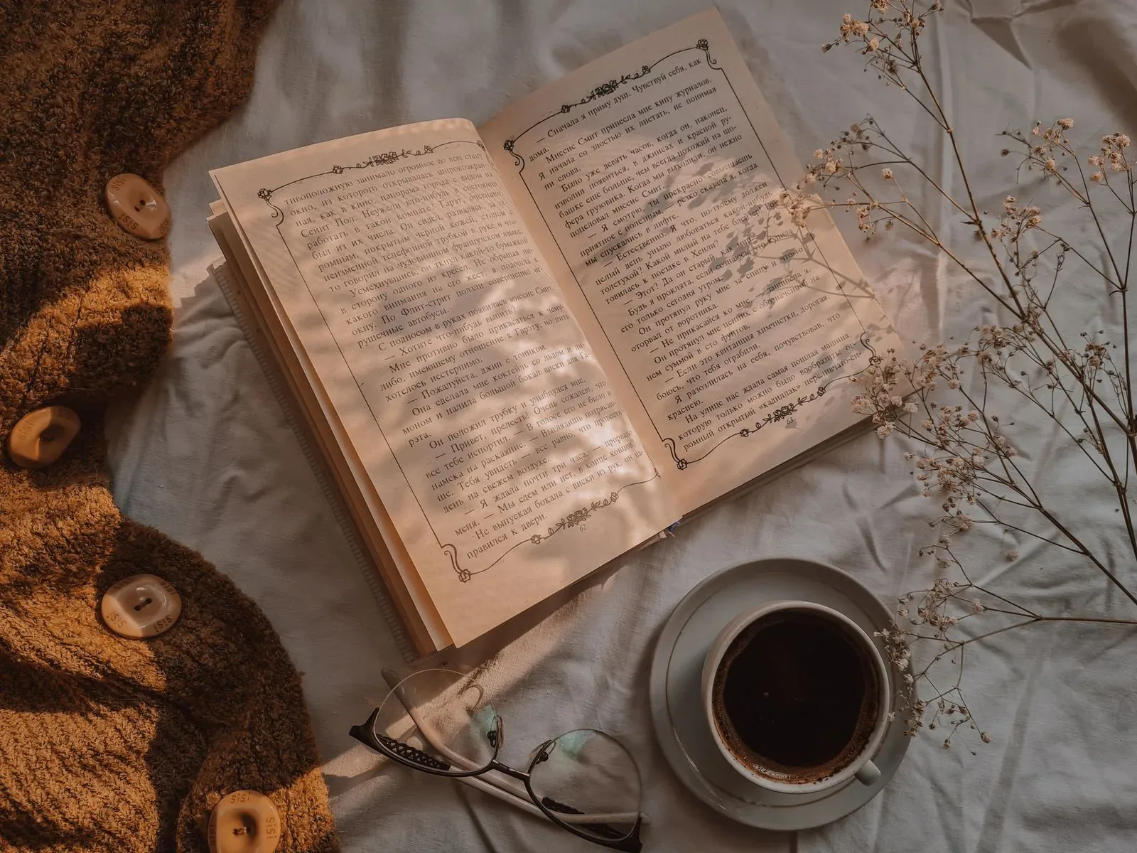 An open book, coffee, flowers, and glasses in warm light